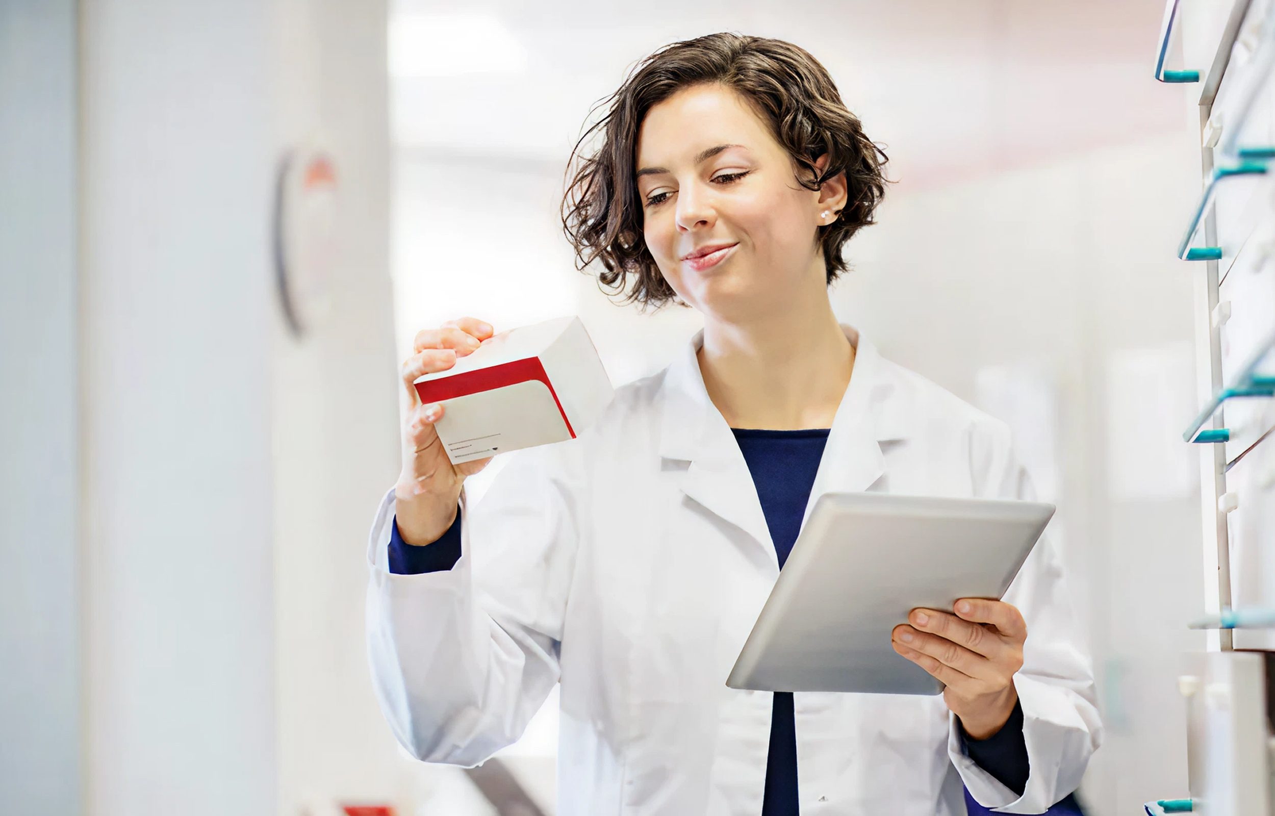Pharmacist holding medication box and tablet in pharmacy setting