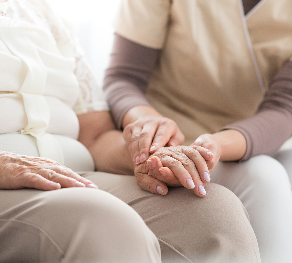 A caregiver’s hands gently holding the hand of an elderly patient.